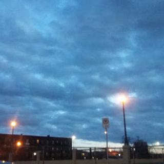 A moody evening sky with scattered clouds and streetlights illuminating the urban landscape.