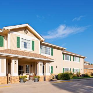 A large two-story residential building with green shutters and beige siding under a clear blue sky.