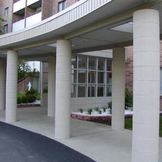 An architectural view of a modern building entrance with columns and landscaped area.