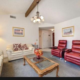 A cozy living room with a mix of white and red furniture, featuring a chandelier and decorative paintings.