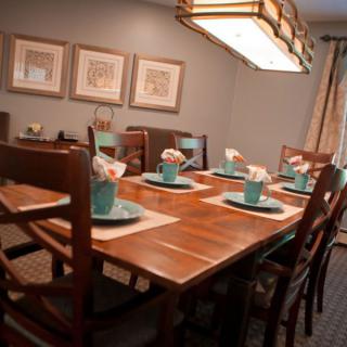 A well-decorated dining room features a wooden table set with turquoise dinnerware and floral arrangements, under a stylish lighting fixture.