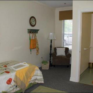 A cozy bedroom interior featuring a bed with colorful bedding, an armchair, a floor lamp, and wall decor.
