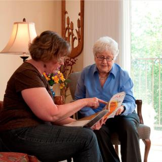 A caregiver assisting an elderly woman with reading in a home setting.