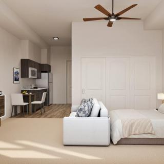 A modern studio apartment interior featuring a bed, kitchenette, and ceiling fan.