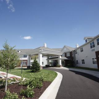 A view of a residential building with a driveway leading to the entrance, surrounded by landscaped greenery under a clear blue sky.