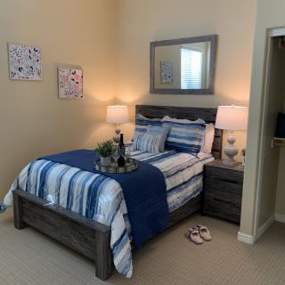 A cozy bedroom with a striped blue and white bedding set, featuring a wooden bed frame, nightstands with lamps, decorative wall art, and a mirror.