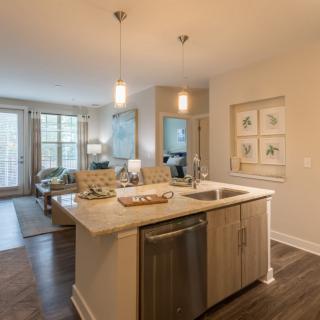 A modern open floor plan featuring a kitchen with an island and pendant lighting, leading into a cozy living room area.
