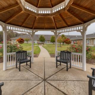 A wooden gazebo with benches overlooks a garden and pathway in an outdoor setting.