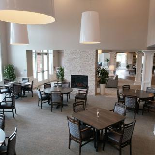 A spacious dining area featuring multiple tables and chairs, large pendant lights, and a central fireplace.