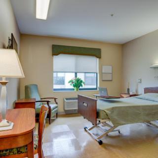 A well-lit hospital patient room featuring a bed, seating area, and window.