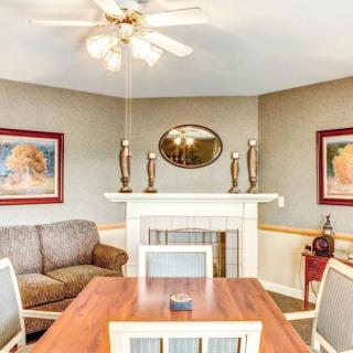 A cozy living room with a combined dining area featuring a wooden table, comfortable sofa, and decorative fireplace adorned with candles and artwork.