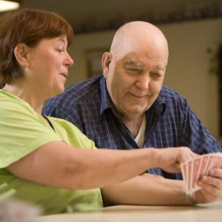 An elderly man and a caregiver playing cards together at a care facility.