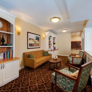 A cozy and elegant living room with a sofa, chairs, bookshelf, and table, featuring warm lighting and decor.