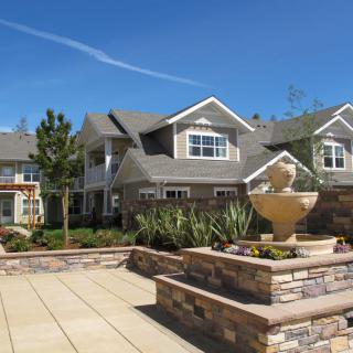 A modern residential building with a landscaped courtyard and fountain under a clear blue sky.
