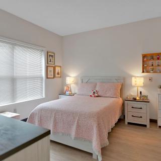 A cozy bedroom with a neatly made bed, flanked by nightstands and lamps, featuring a large window and tasteful decor.