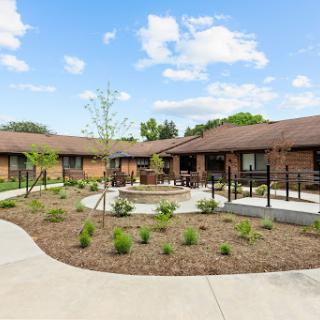 A well-designed courtyard featuring single-story brick buildings, surrounded by lush landscaping and a blue sky.