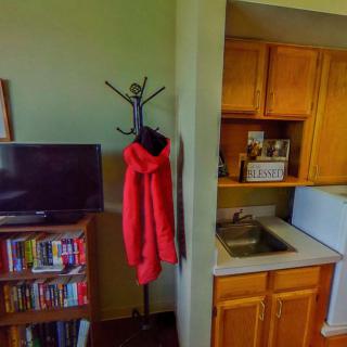 A cozy living area with a kitchenette, TV, bookshelf, and red coat on a rack.