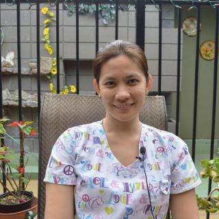 A woman smiling while sitting outdoors in a garden setting.
