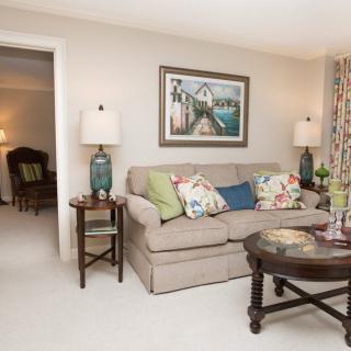 A cozy living room featuring a sofa with colorful pillows, framed artwork, and elegant lamps on side tables.