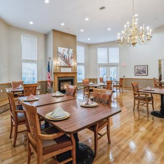 A spacious dining room with neatly arranged tables and chairs, illuminated by a chandelier.