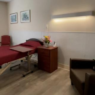 A tidy hospital room featuring a bed, bedside table, and comfortable chair.