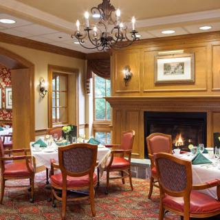 Elegant dining area with a fireplace and chandelier, featuring classic wooden decor and neatly set tables.