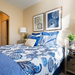 A cozy bedroom features a blue and white color scheme with ornate patterns on the bedding, complemented by framed artwork and plants.