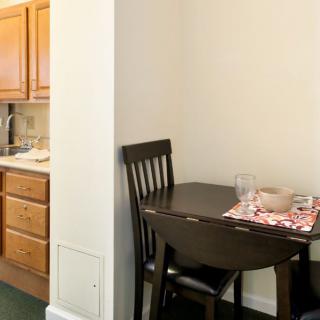 A cozy dining nook adjacent to a small kitchen area, featuring a wooden table set for two.
