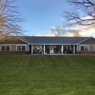 A suburban house with a large lawn and a porch, surrounded by bare trees under a clear sky.