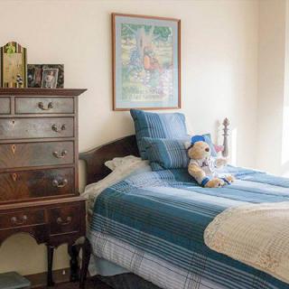 A cozy bedroom featuring a neatly made bed with a teddy bear on top and a wooden dresser in the corner.
