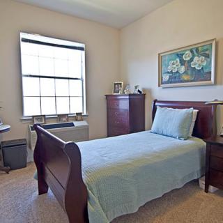 A cozy bedroom featuring a single bed, desk, and dresser with a large window and artwork on the wall.
