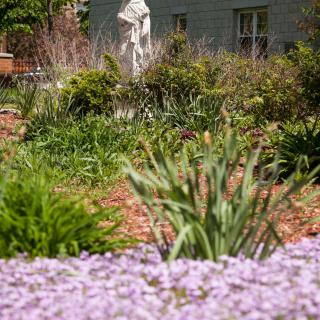 A serene garden with blooming flowers and a statue in the background.