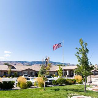 A scenic view of a building with an American flag, lush greenery, and mountains in the background under a clear blue sky.