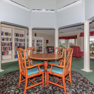 A cozy library with a round table surrounded by wooden chairs, featuring bookshelves and comfortable seating.