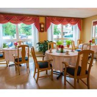 A cozy dining room with round tables, wooden chairs, and large windows adorned with elegant curtains.