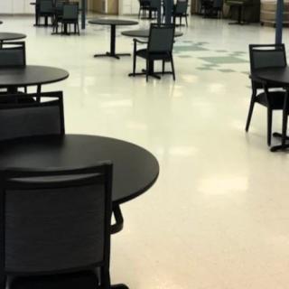 An empty cafeteria with tables and chairs arranged across the floor.
