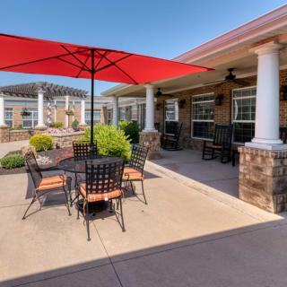A sunny outdoor patio with a red umbrella and seating area.