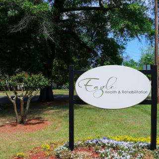 A sign for a business named 'Eagle Health & Rehabilitation' surrounded by greenery and flowers.