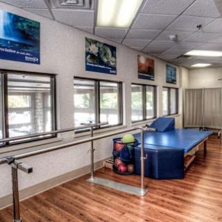 A spacious physical therapy room equipped with a barre, colorful exercise balls, and large windows allowing natural light.