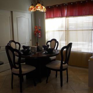 A cozy dining room with a round table and elegant chairs, illuminated by a decorative chandelier with natural light filtering through the window blinds.