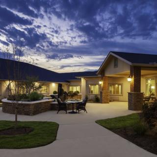 A well-lit building exterior at dusk, featuring a courtyard and landscaped surroundings.