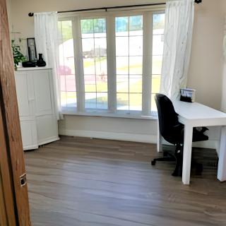 A minimalist home office with a desk and chair by a large window, allowing natural light to fill the room.