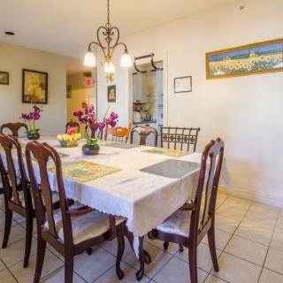 A warmly lit dining room featuring a large table with a white tablecloth, surrounded by wooden chairs and adorned with decorative elements like flowers.