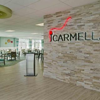 A modern restaurant interior with a stone wall featuring the Carmella logo and an inviting dining area in the background.