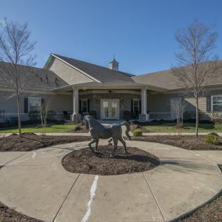 A building entrance with a horse statue in the foreground and landscaped surroundings.