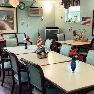 A cozy dining room with several tables and chairs, adorned with flower arrangements and American flags.
