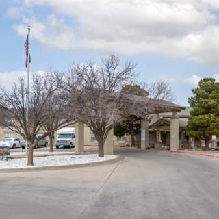 A building entrance with a driveway lined by trees and a flagpole under a cloudy sky.