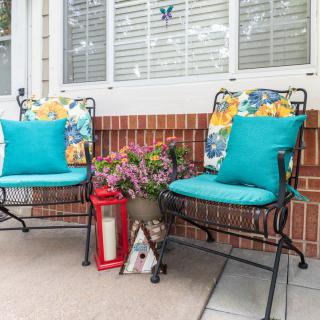 A cozy patio setup featuring two chairs with colorful cushions, a decorative lantern, and a pot of flowers against a brick wall.