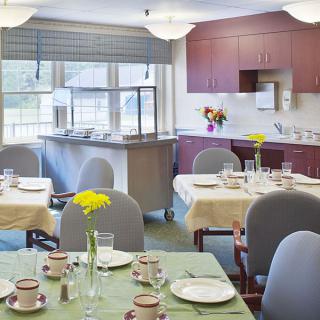 A cozy dining area with set tables and a kitchen in the background.