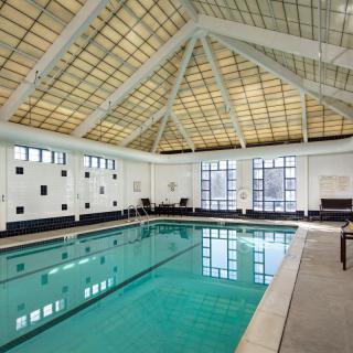 A spacious indoor swimming pool with a high, grid-patterned ceiling and large windows allowing natural light to flood the area.